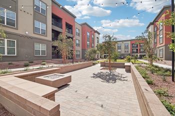 an outdoor area with benches and trees in front of an apartment building at The Maddox Luxury Apartment Homes, Buckeye, AZ